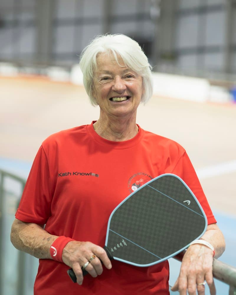 Elinde pickleball raketiyle gülümseyen beyaz saçlı bir kadın